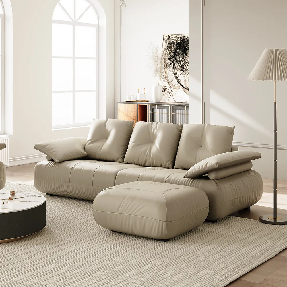 Modern beige leather sofa with plush cushions and ottoman in a bright minimalist living room featuring arched windows and neutral decor