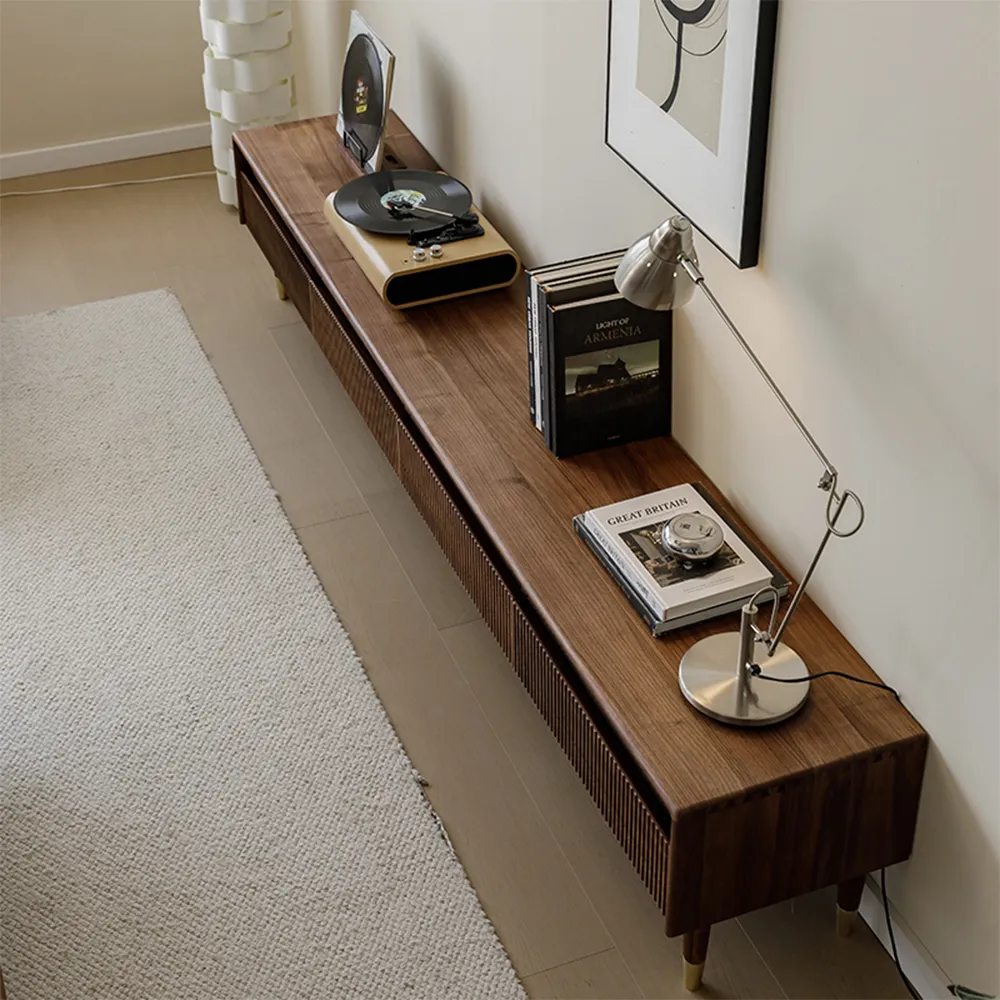 Long walnut TV console with slatted doors, styled with books, a turntable, and a modern desk lamp in a minimal neutral-toned living room.