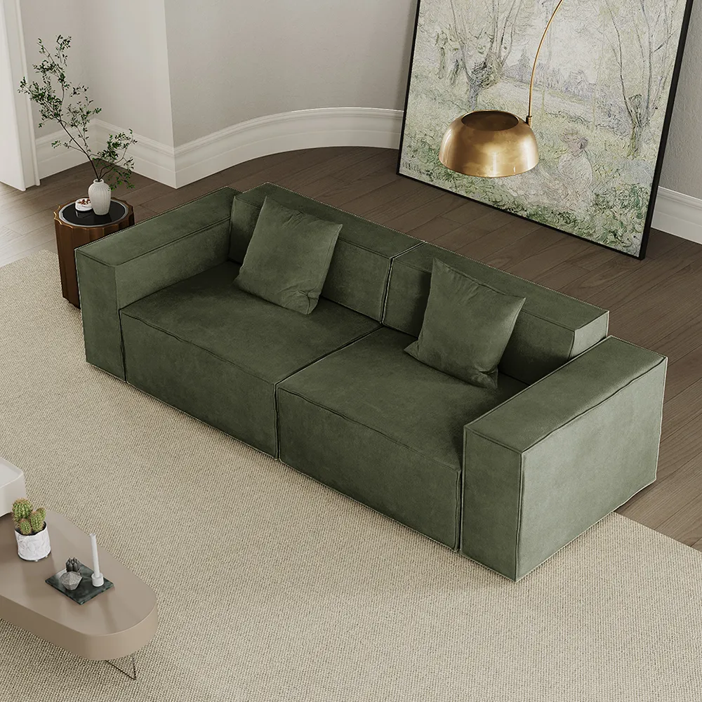 Deep green boxy modular sofa with wide armrests and minimalist cushions, styled in a modern white-walled interior with wooden floors

