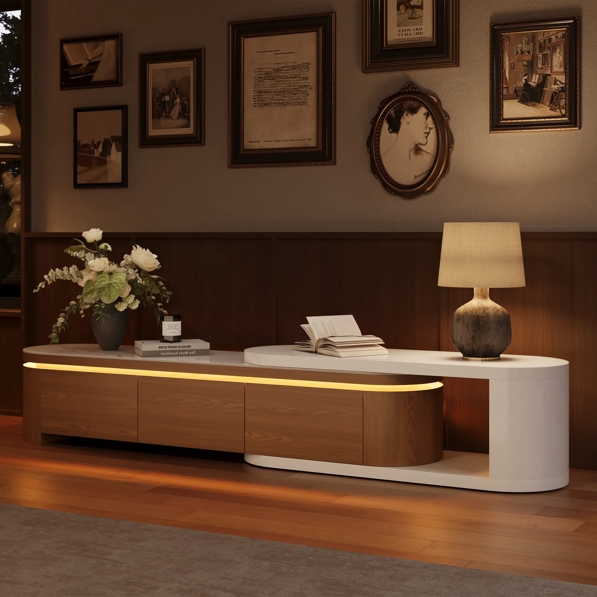 Alt: Curved modern TV console with white and wood finishes, featuring built-in LED lighting, a decorative lamp, books, and wall art in a vintage-inspired interior.