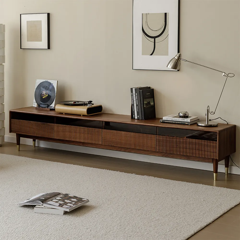 Long walnut TV console with slatted doors, styled with books, a turntable, and a modern desk lamp in a minimal neutral-toned living room.