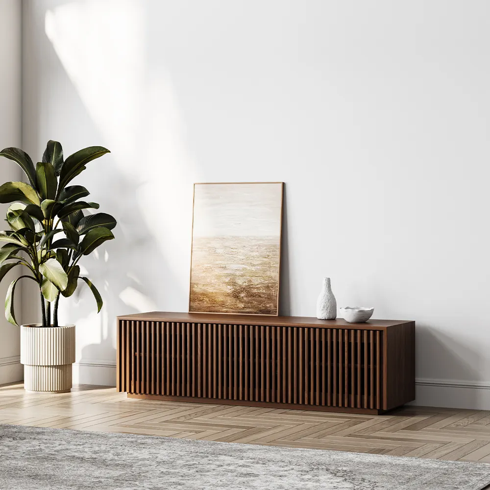 Low-profile modern wood TV console with vertical slat detailing, staged against a white wall with natural light and minimalist ceramic accents