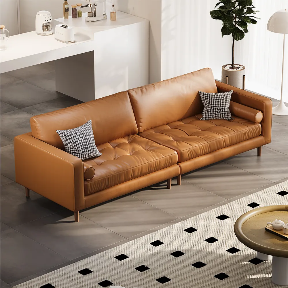 Modern caramel brown leather sofa with tufted seating and minimalist armrests, styled in an open-plan living space