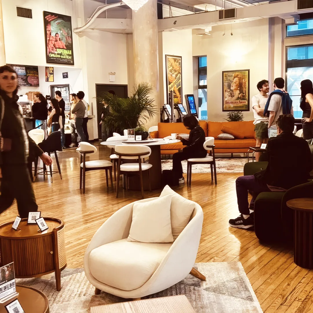 Modern furniture showroom with visitors interacting around a round dining table, accent chairs, and a cozy beige lounge chair on a rug.