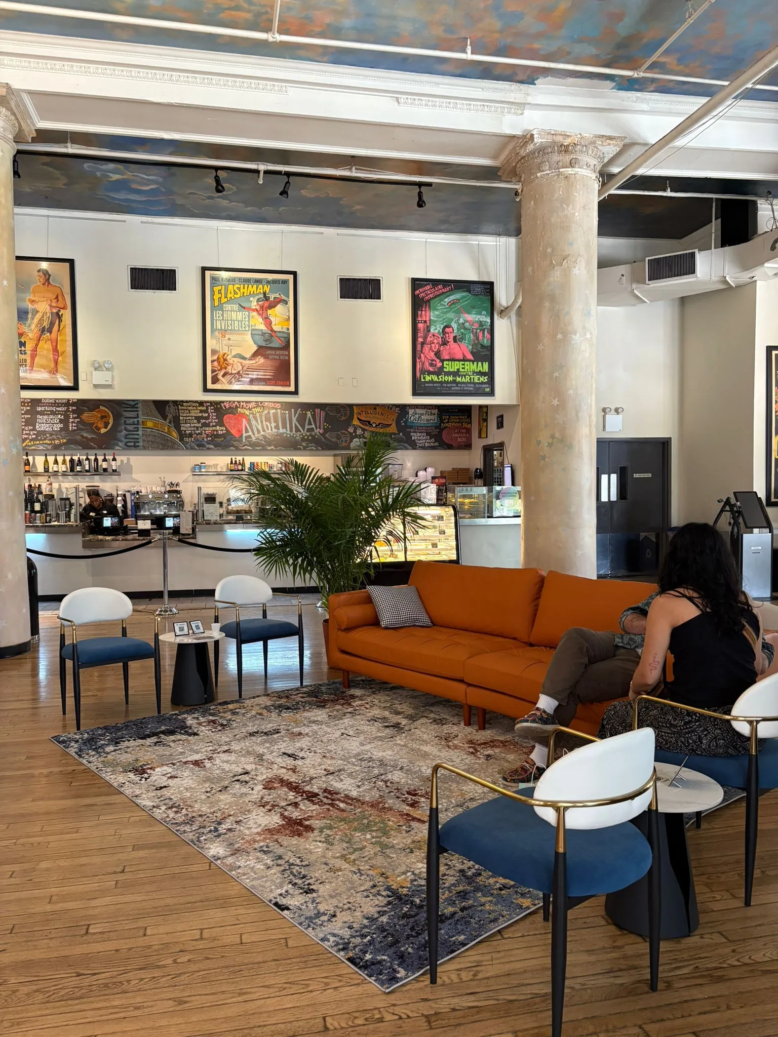Modern furniture showroom with visitors interacting around a round dining table, accent chairs, and a cozy beige lounge chair on a rug.