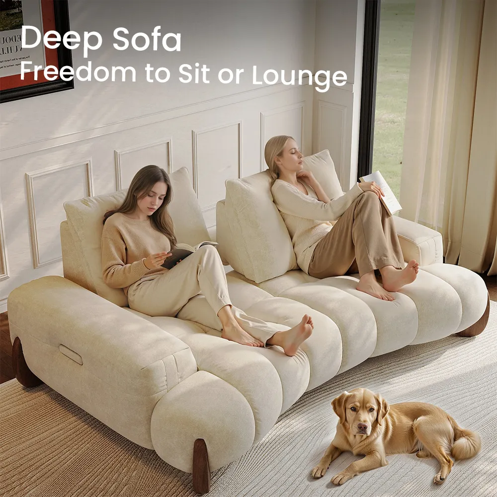 Two women relaxing on a cream-colored deep sofa with oversized cushions, one reading and one lounging, in a bright living room with a golden retriever lying nearby.