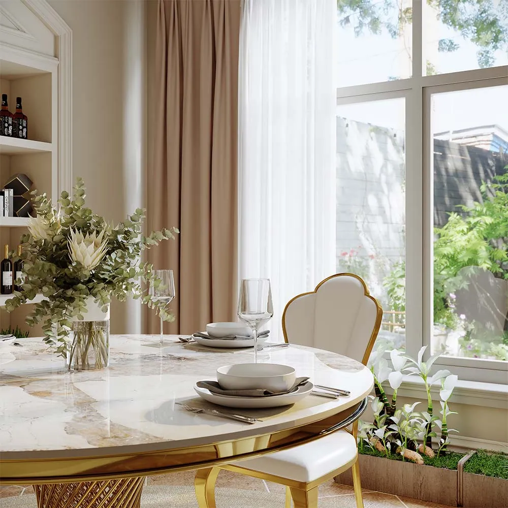 Close-up of an elegant marble round dining table with gold trim, styled with floral centerpiece and fine tableware near a sunny window.