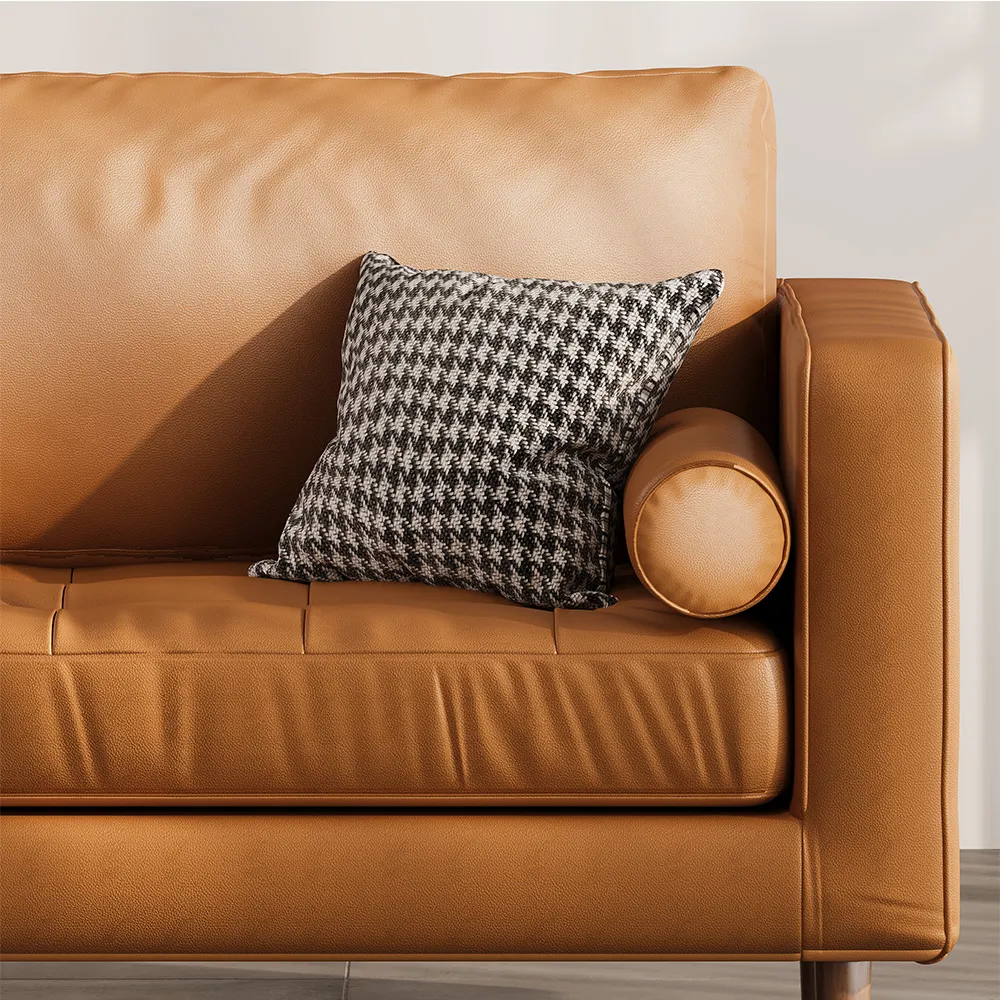 Close-up of brown leather sofa armrest with hounds-tooth throw pillow and matching round bolster cushion