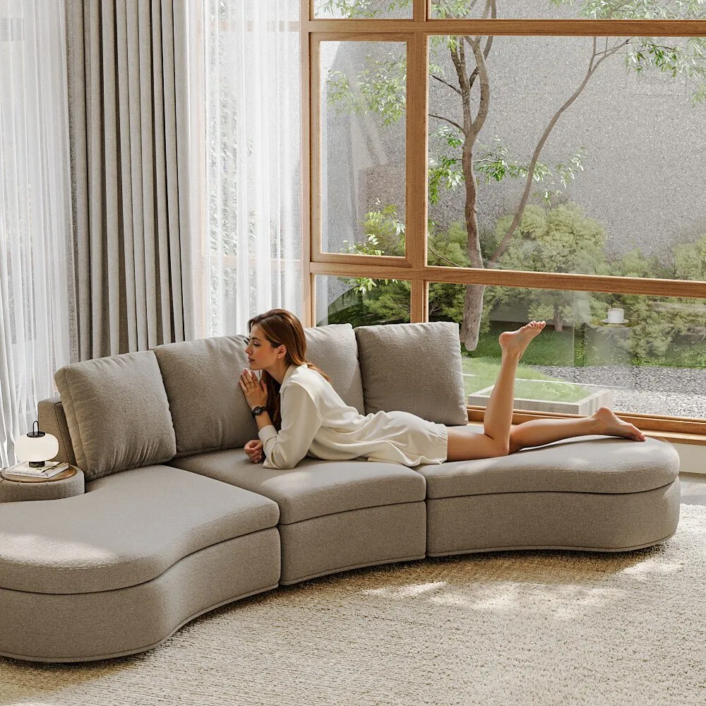 Modern curved beige modular sofa with side tables in a bright living room, featuring a large window and natural light