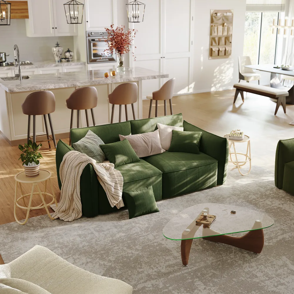 Green corduroy sofa with plush cushions in an open-concept living and kitchen area, surrounded by soft lighting and neutral-toned furniture.