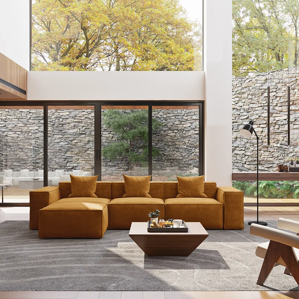 Modern modular fabric sofa in warm mustard color with chaise, styled in a spacious living room with floor-to-ceiling windows and a gray area rug