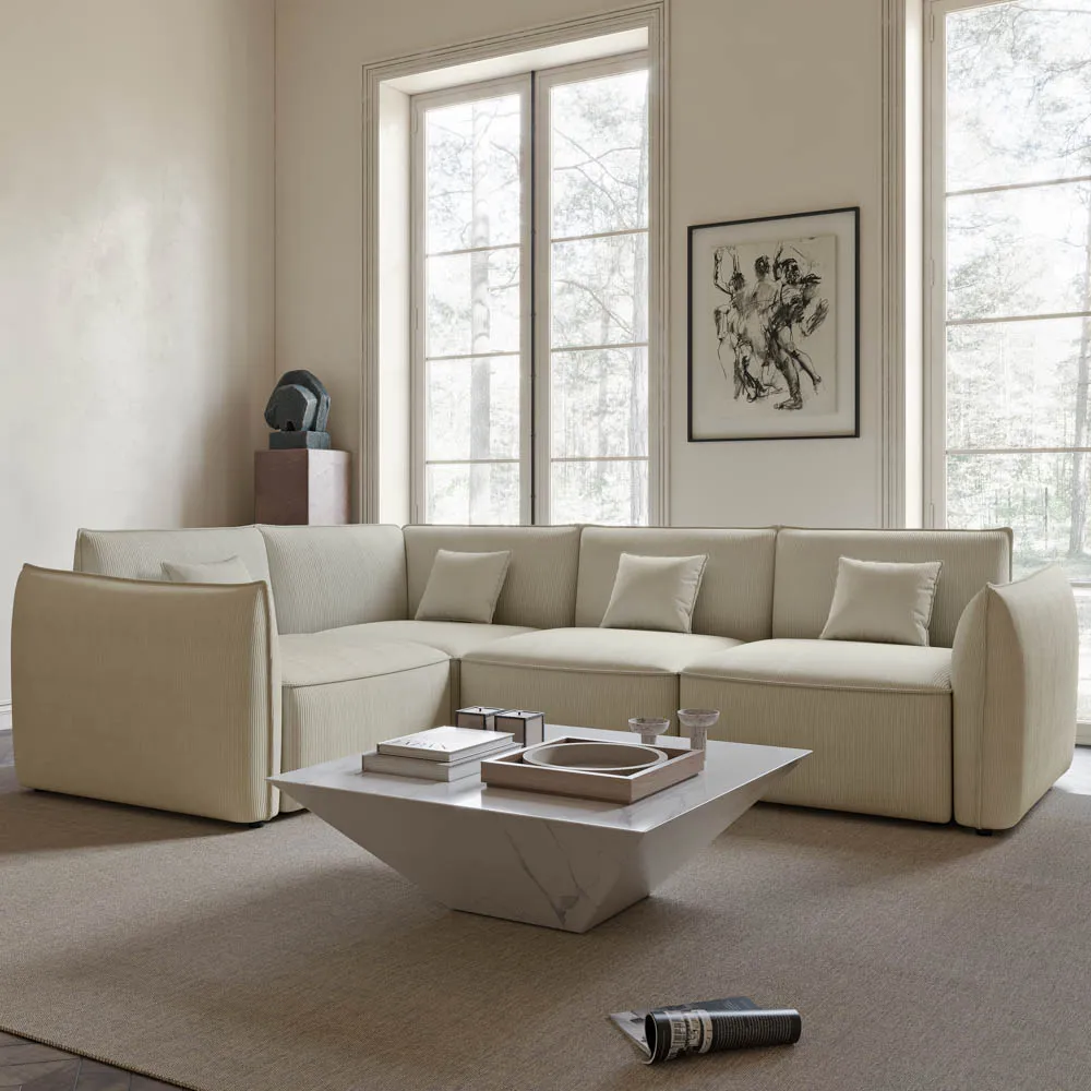 Modern cream-colored L-shaped sectional sofa in a minimalist living room with large windows and a marble coffee table