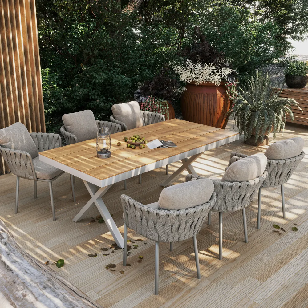 Outdoor dining set with rope-woven cushioned chairs and wooden table on a patio surrounded by greenery