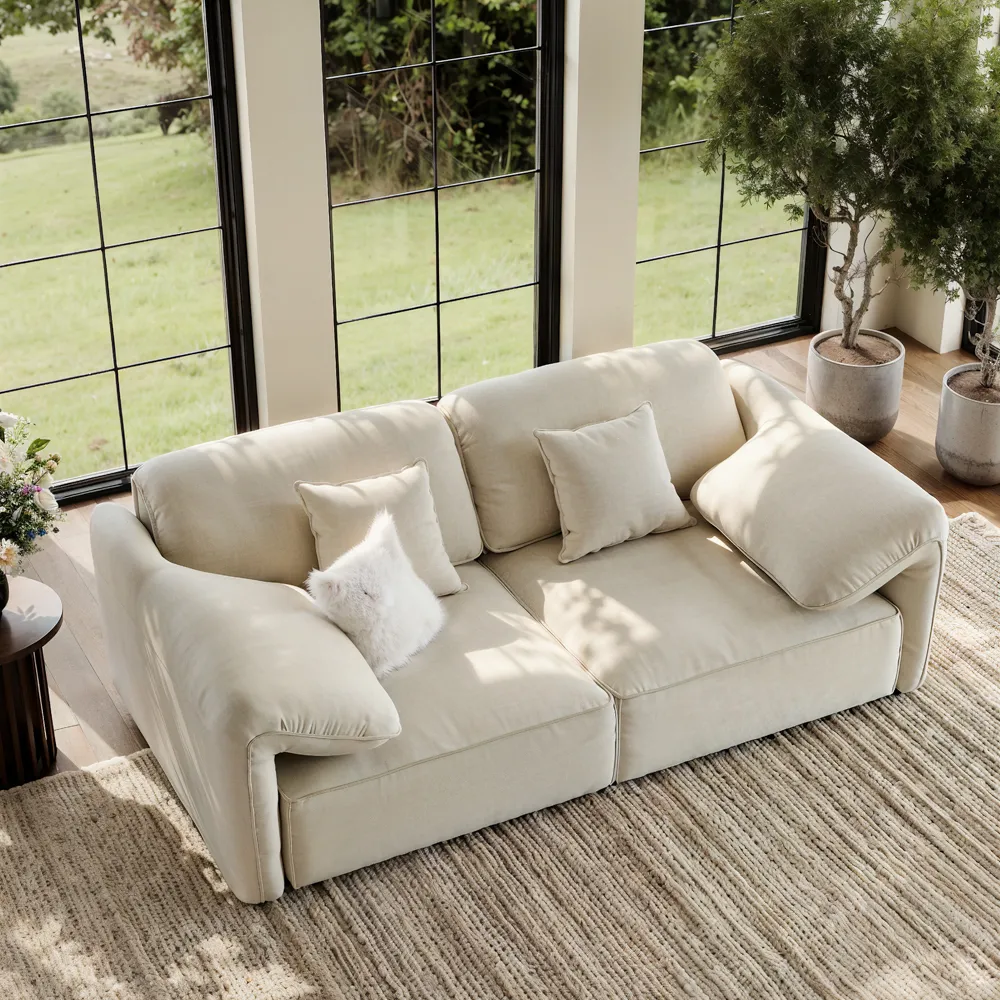 Beige 2-3 seater modern sofa with soft curved arms, displayed in a bright room with large windows and natural light