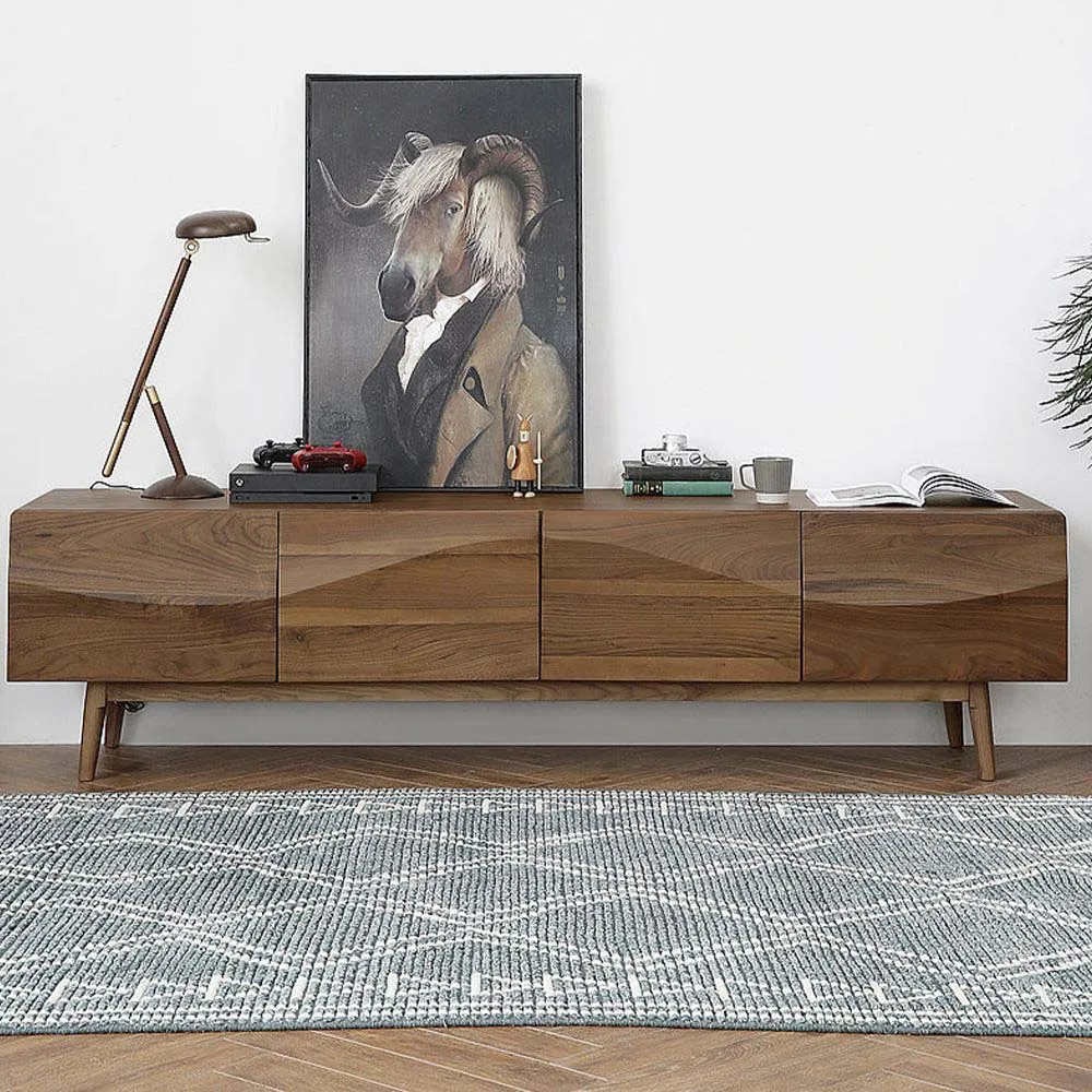 Mid-century walnut TV stand with angled legs and geometric carved drawer fronts, displayed in a bright minimalist room