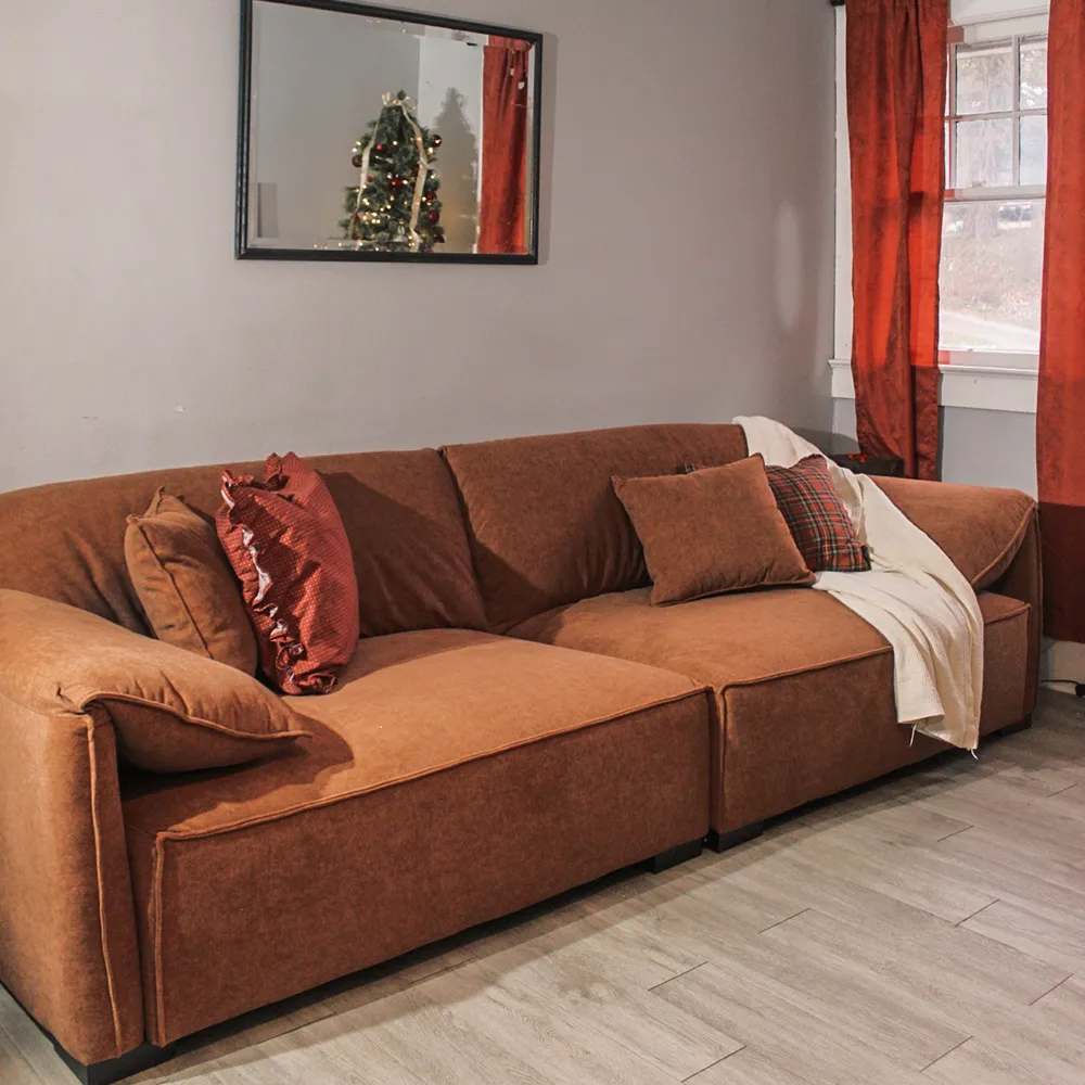 Rust-colored deep seat sofa with plush cushions and textured pillows, set against a gray wall with a mirror and holiday reflection.