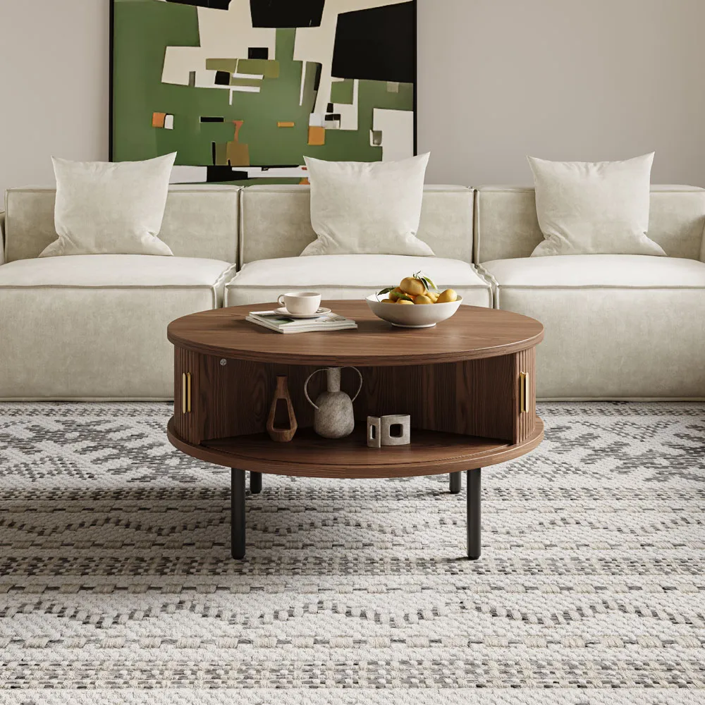 Round walnut coffee table with brass accents and open shelf, styled in front of a cream modular sofa on a patterned rug.