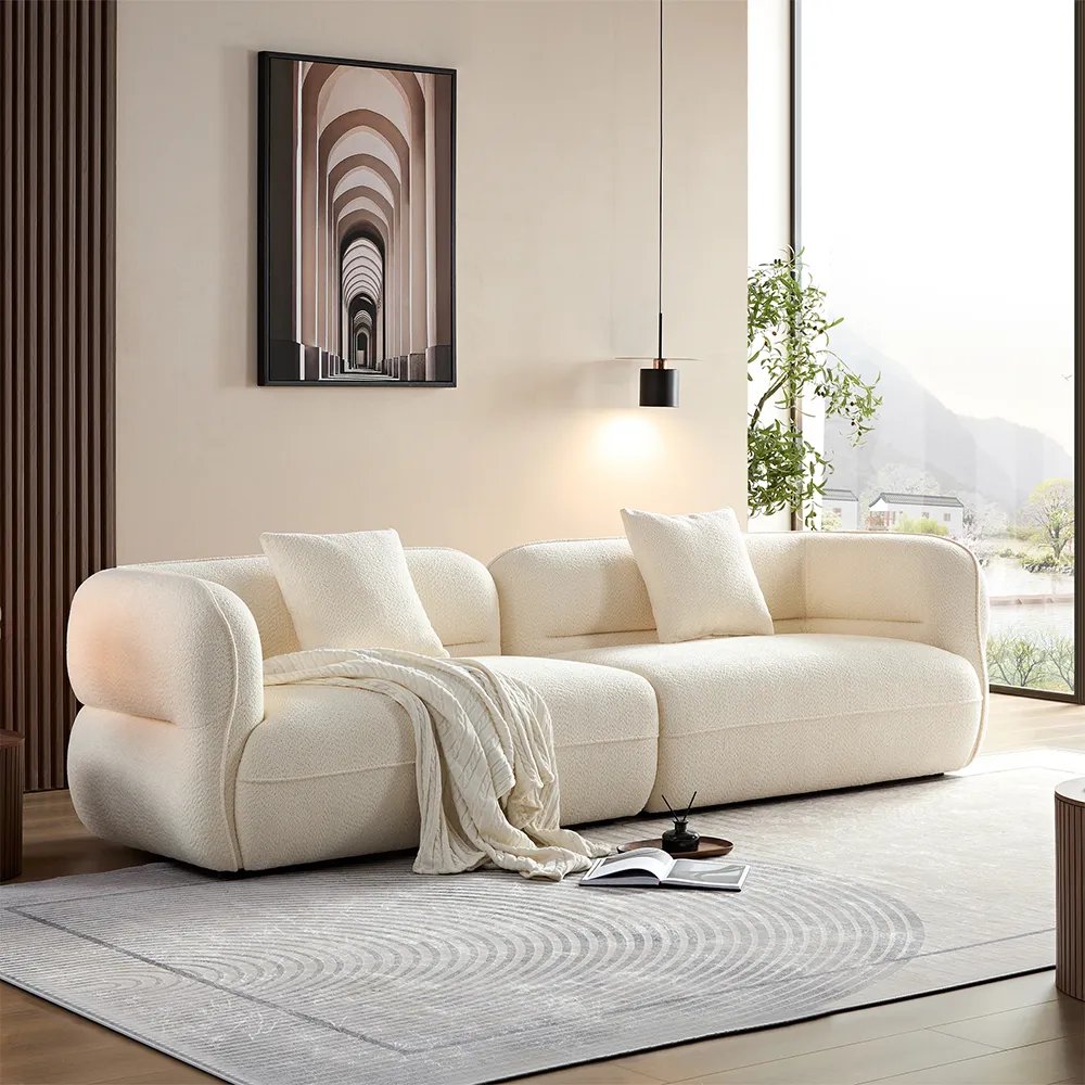 Minimalist living room featuring a white curved boucle sofa with soft cushions and throw blanket, set beside large windows and modern wall art