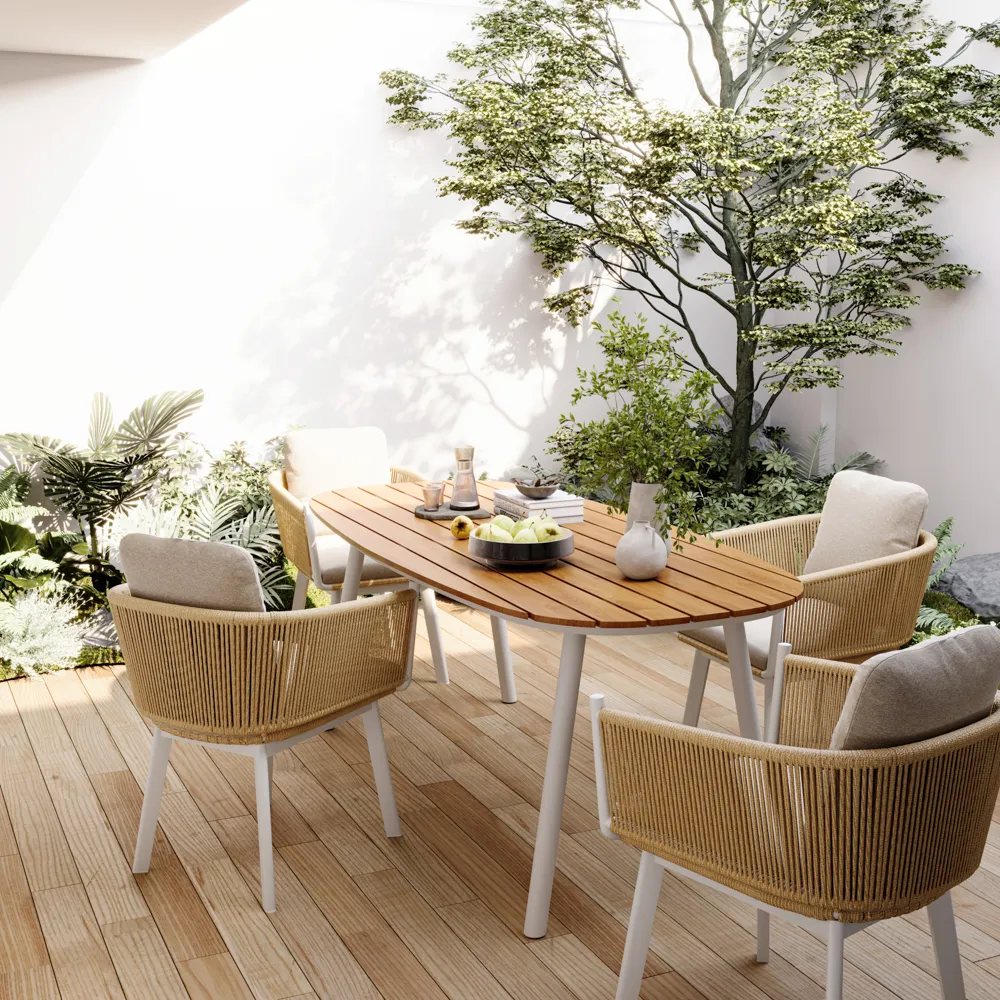 Open-air patio setup with teak wood table and cushioned rope chairs, bathed in natural sunlight and framed by leafy plants.