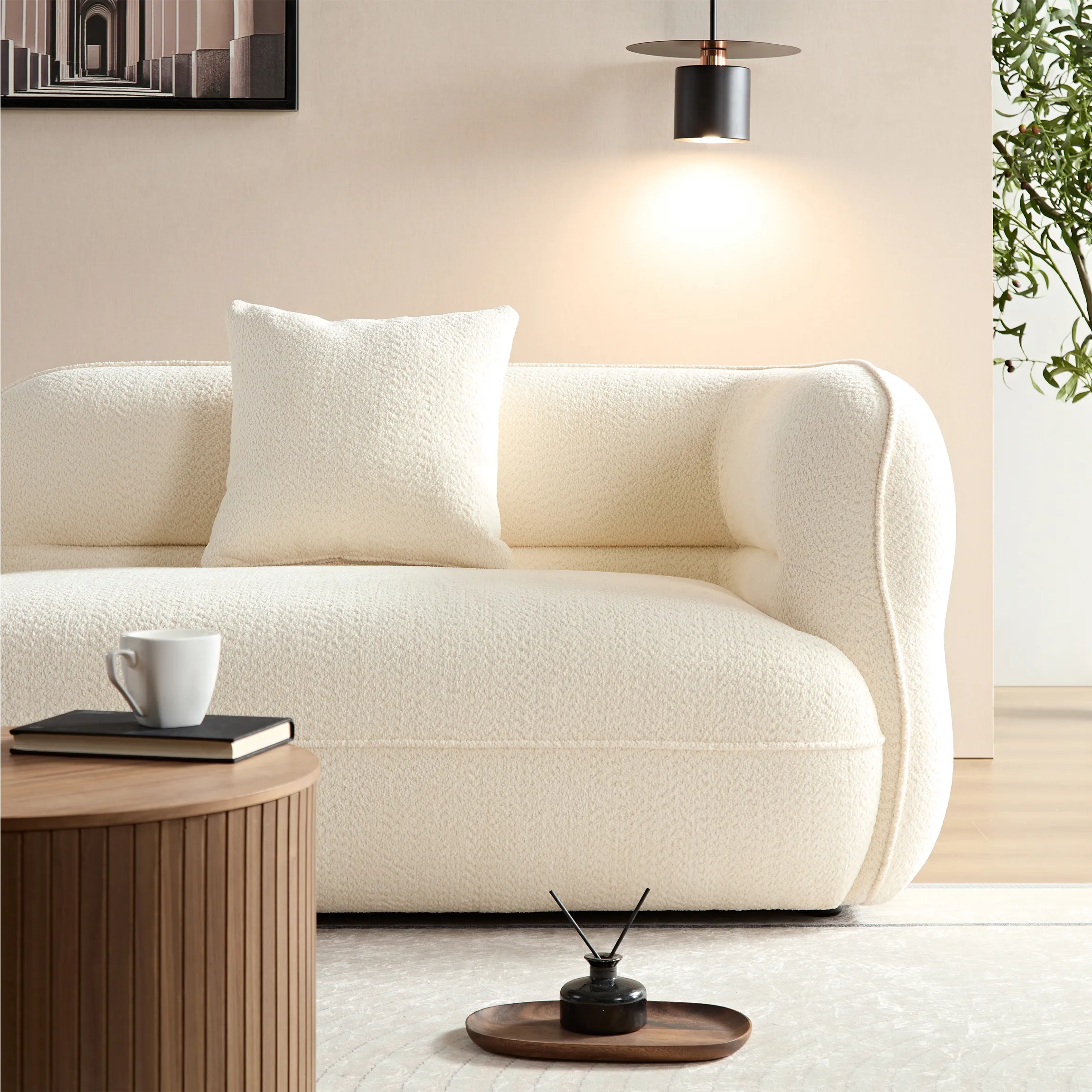 Close-up of a modern white curved sofa with boucle fabric texture, accented by a matching pillow and ambient wall lighting