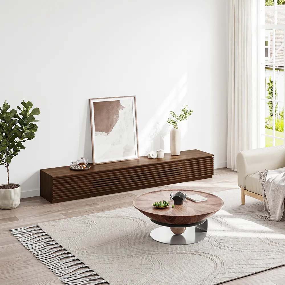 Low-profile walnut slatted TV cabinet paired with round wood coffee table, styled in a bright modern living room with large windows and indoor greenery
