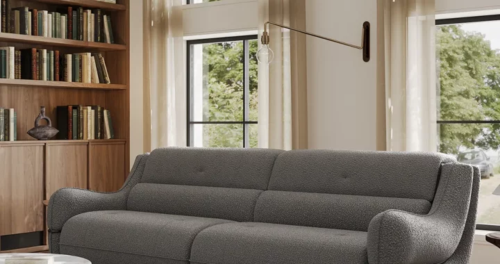 Charcoal gray boucle sofa with rounded armrests in a tall-windowed library room, styled with wooden bookshelves and marble coffee table
