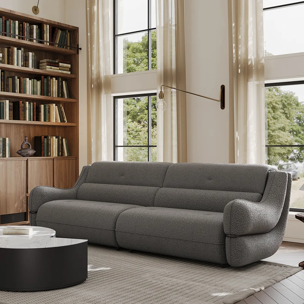 Charcoal gray boucle sofa with rounded armrests in a tall-windowed library room, styled with wooden bookshelves and marble coffee table