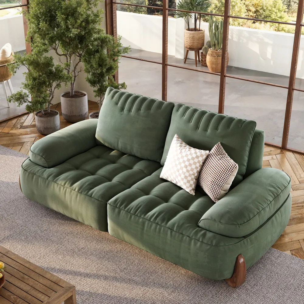 Tufted green velvet sofa with plush arms and wooden legs, paired with checkered throw pillows in a sunlit room featuring potted plants and wood flooring.