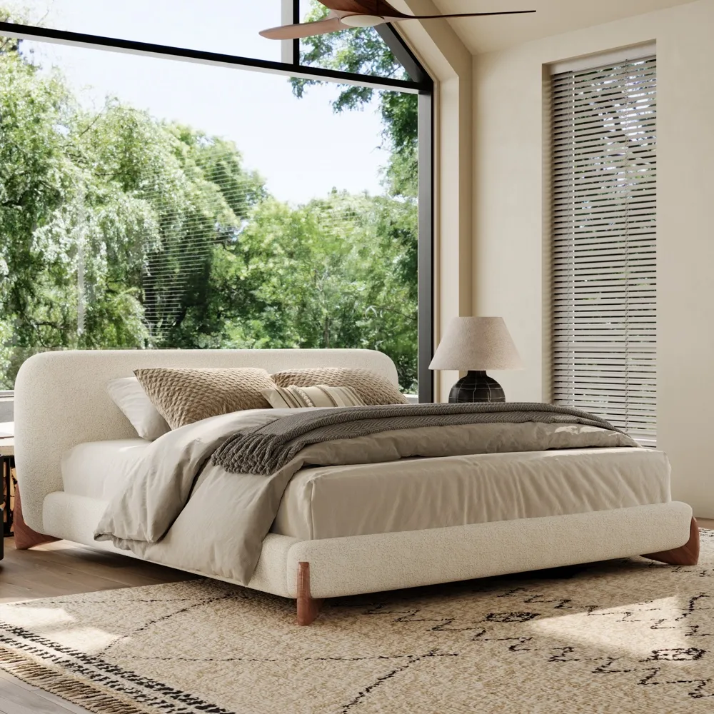  Modern queen size boucle upholstered bed with rounded headboard and wooden legs in a sunlit bedroom with large glass window