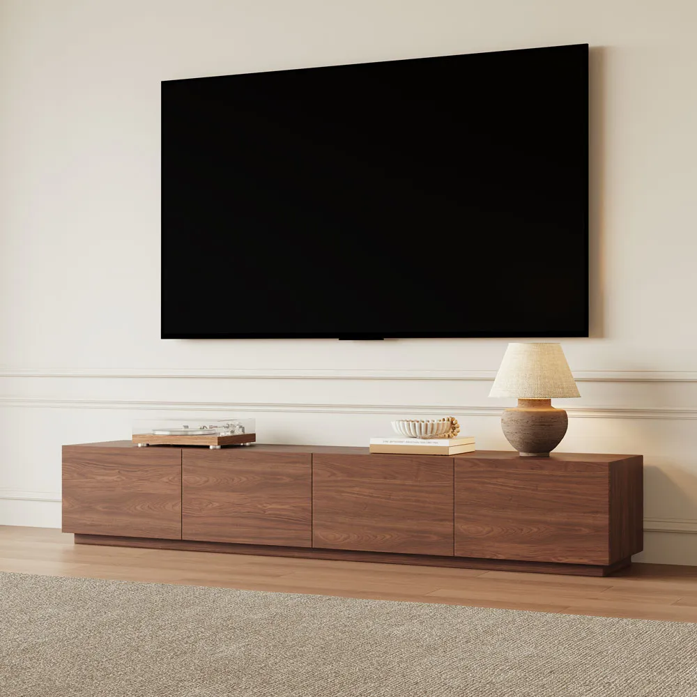 Minimalist wood TV stand with three-panel front design, styled with a ceramic lamp, books, and a record player, positioned under a wall-mounted flat screen.
