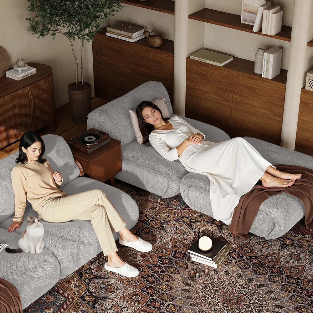 Two women relaxing on a modern gray sectional sofa in a mid-century inspired living room with a patterned rug and wooden shelves
