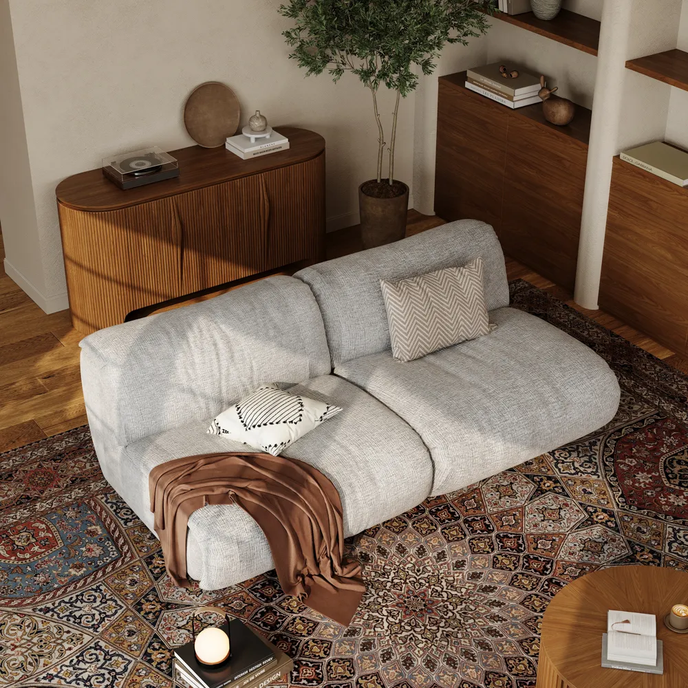 Light gray modular armless two-seater sofa styled with patterned pillows and throw blanket, placed on a vintage rug in a modern living space.