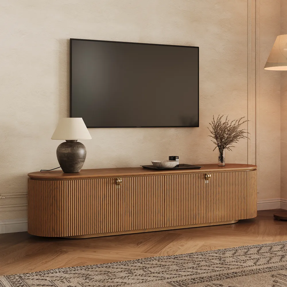 Mid-century modern fluted TV stand with curved edges, brass handles, and walnut finish, placed in a minimalist living room under wall-mounted TV.