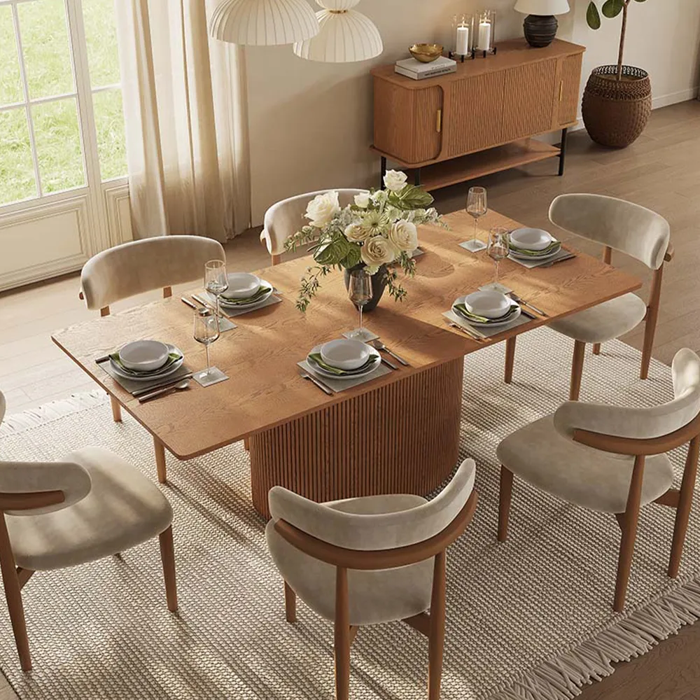 Mid-century modern rectangular dining table with fluted pedestal base and walnut wood grain, styled with cream velvet chairs in a sunlit dining room.