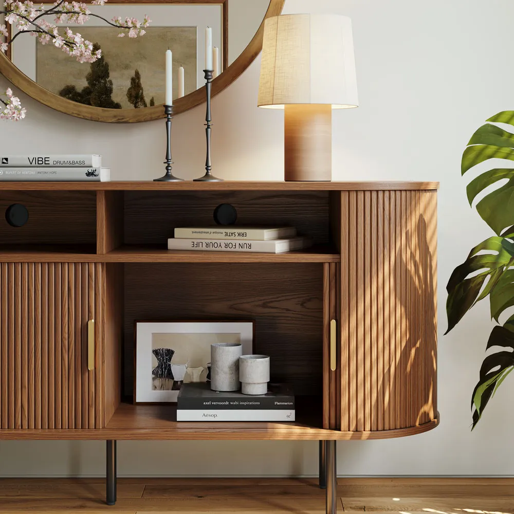 Close-up of mid-century fluted sideboard showing open cabinet storage with books, candles, and framed artwork on walnut shelves.