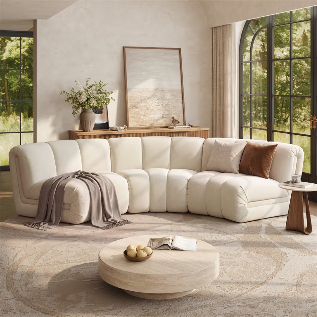 White curved modular sectional sofa with plush cushions in a bright modern living room with large arched windows.