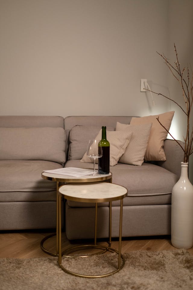 A Wine Bottle and a Wine Glass on a Round Table Beside a Sofa