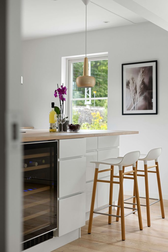 A kitchen with white cabinets and stools next to a window