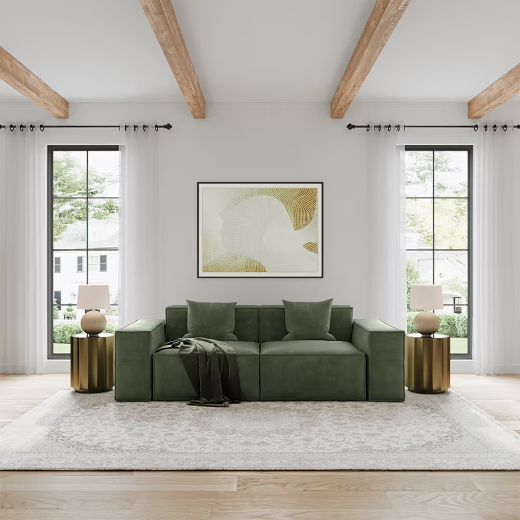 Green modular sofa with wide track arms and throw pillows in a bright living room with exposed wood beams.