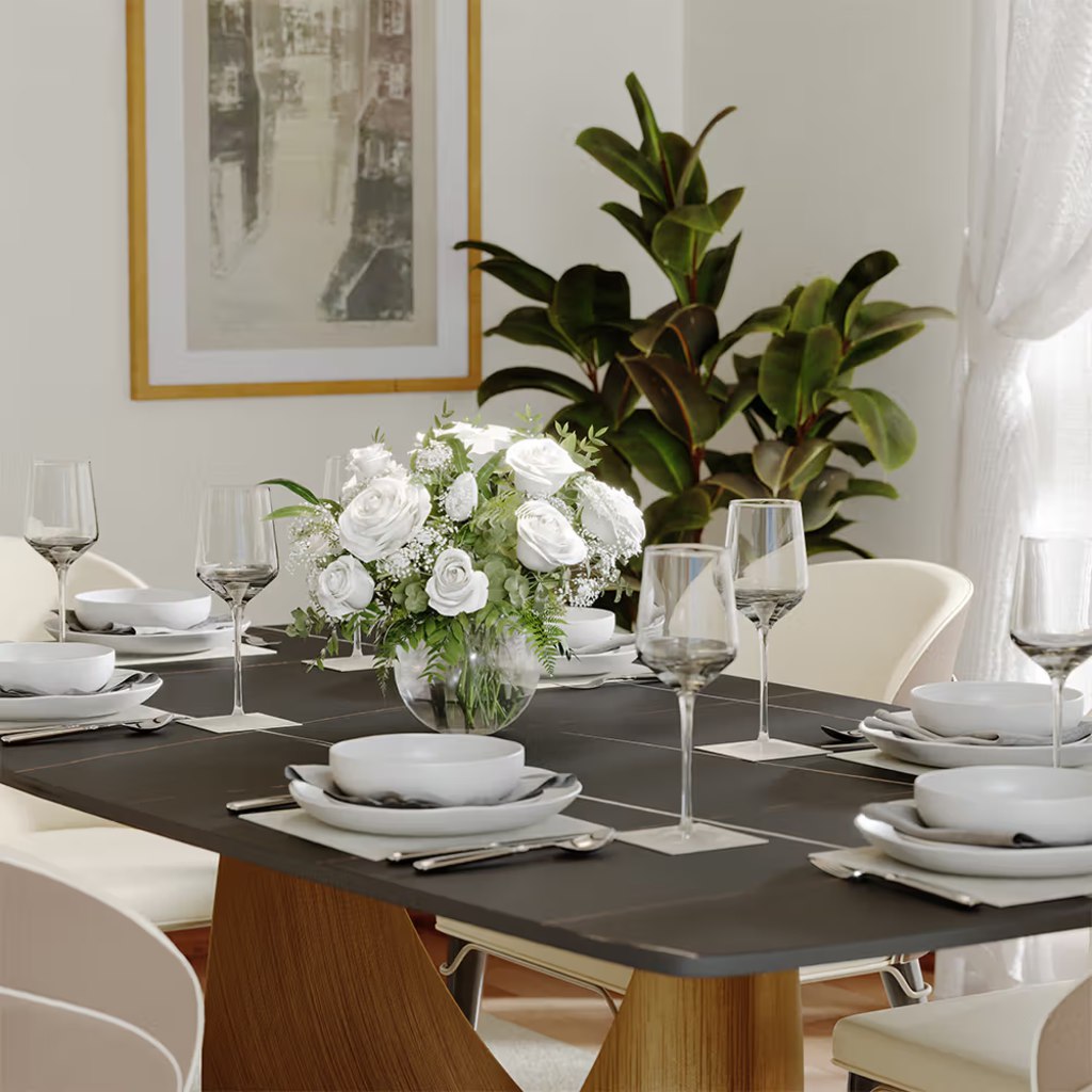 Black rectangular dining table set for eight with white chairs, place settings, and a floral centerpiece in a bright dining room.