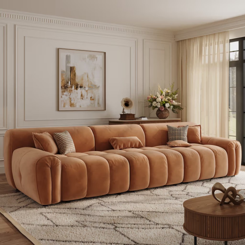 Orange velvet deep-seat sofa with channel-tufted cushions and rounded arms in a bright contemporary living room.
