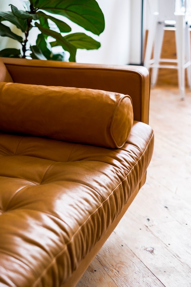 Close-up of a tan leather sofa with tufted seat cushion and cylindrical bolster pillow in a modern living room