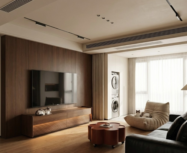 Stylish modern tv stand integrated into wooden accent wall, large TV mounted above cabinet, cats relaxing, beige bean bag chair, washer-dryer unit, and track lighting in modern apartment.