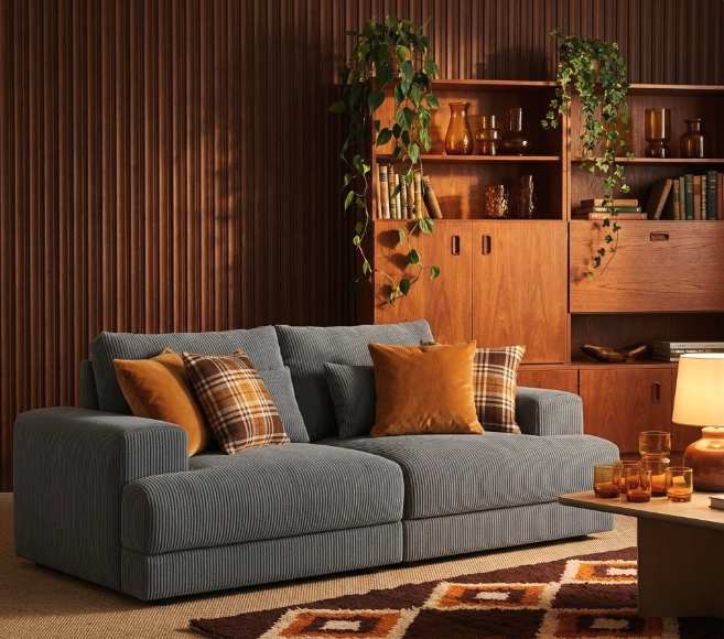 Explore how to style grey sofa in mid-century modern style using mustard yellow and plaid throw pillows, wooden slatted wall, retro cabinet with trailing plants, amber glass accessories, and geometric patterned rug for cozy retro vibe.