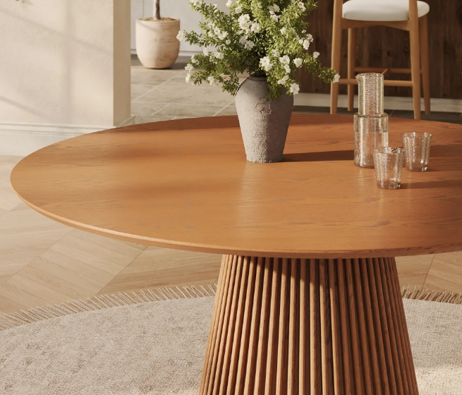 Beautiful modern dining table showcasing a smooth round oak wood top on a tall, sculptural fluted wooden pedestal base, perfect for warm minimalist and organic interiors.