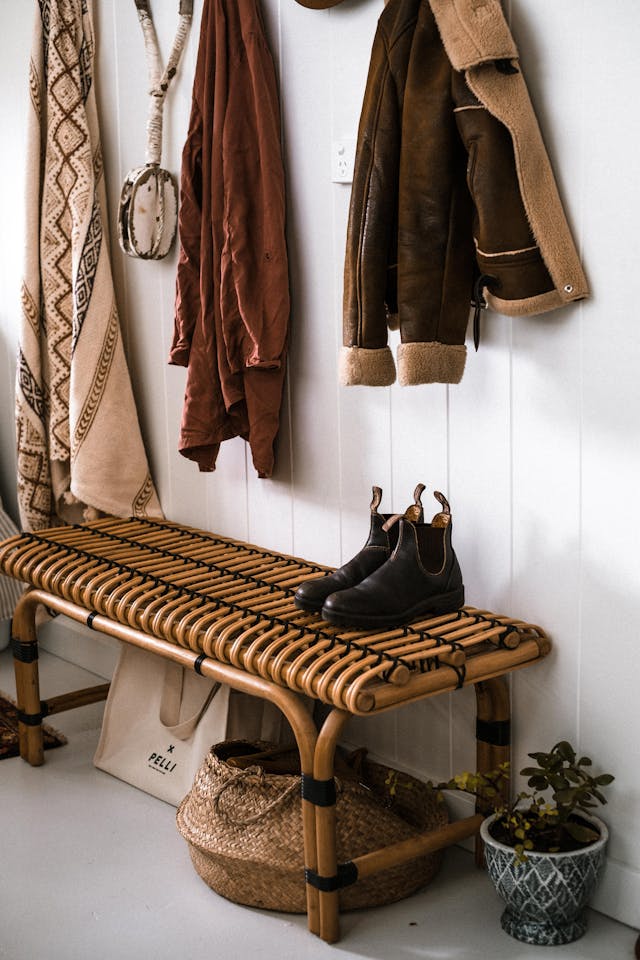 Warm rustic entryway with a woven bench, plants, boots, and layered textiles, showing a cozy bench styling idea.