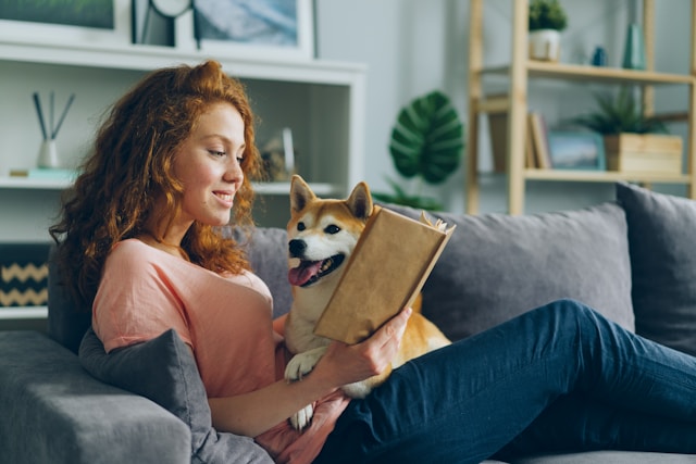 Woman sitting on a couch reading with her dog beside her