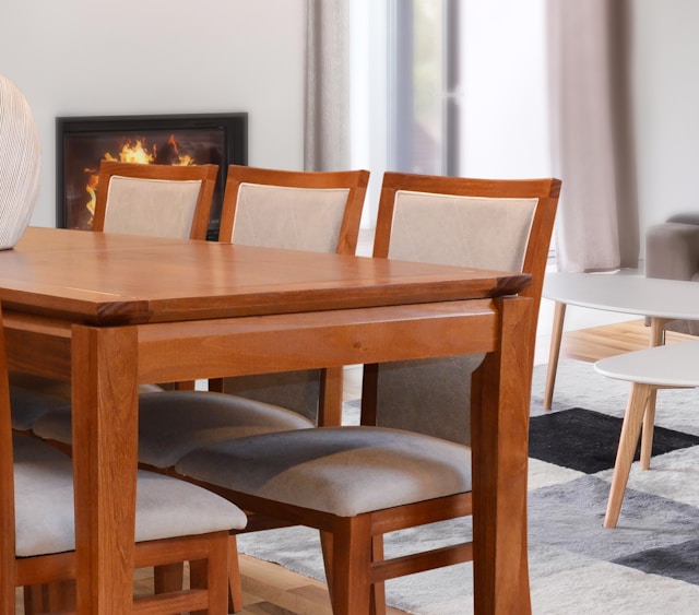 Wooden dining table with upholstered chairs and fireplace.