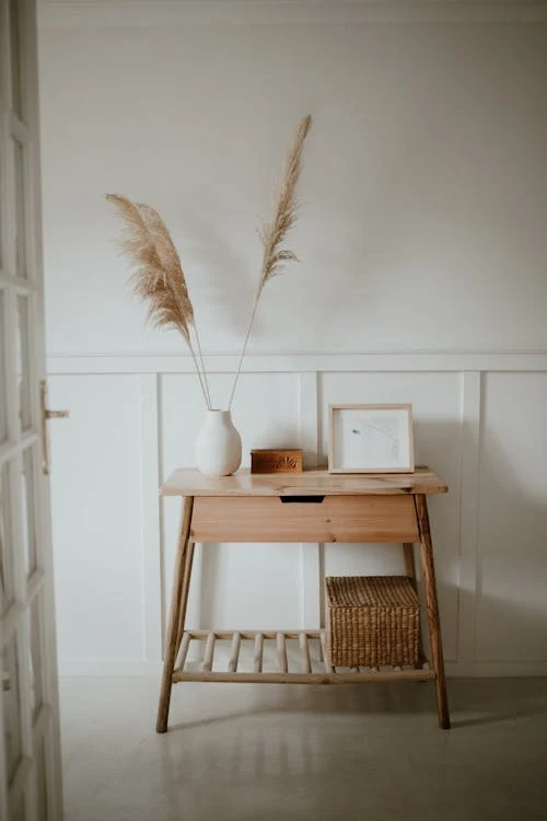 minimalist light wood console table with one drawer, slatted shelf and woven basket in a white entryway