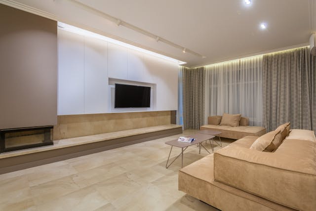 Minimalist beige living room with wall-mounted TV above a long low TV stand and sectional sofa, illustrating proper TV stand width and height for large screen